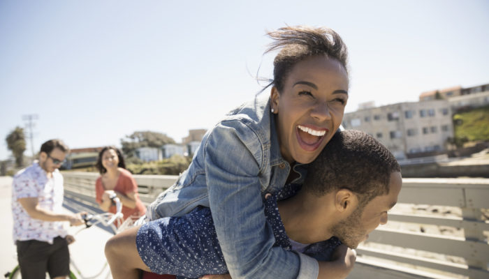 Playful couple piggybacking on sunny sidewalk Playful couple piggybacking on sunny sidewalk