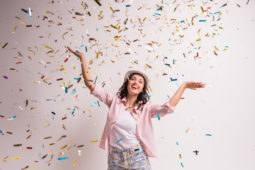 Cheerful young woman is stretching out her hands while confetti falling on her.