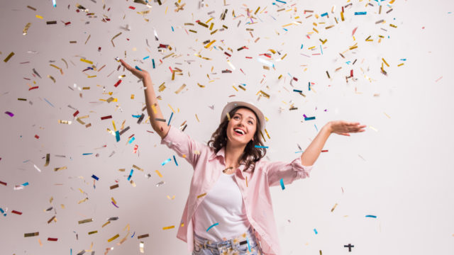 Cheerful young woman is stretching out her hands while confetti falling on her.